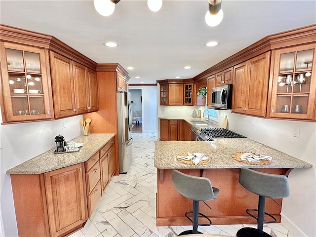 kitchen with light stone countertops, brown cabinetry, a peninsula, recessed lighting, and stainless steel appliances