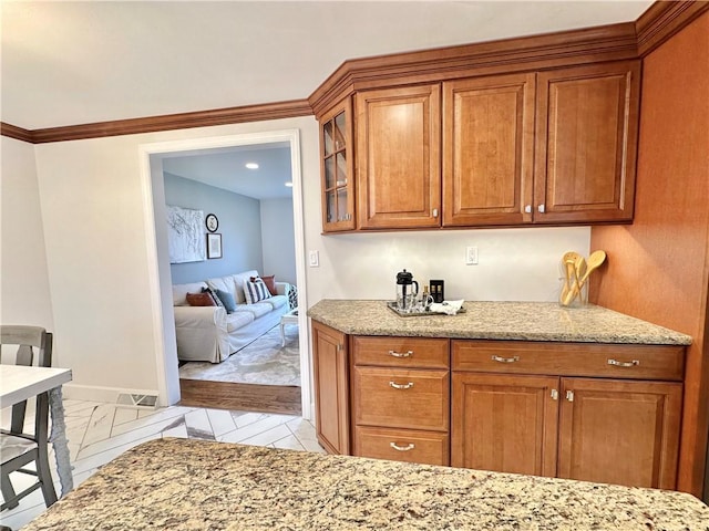 kitchen with glass insert cabinets, brown cabinetry, light stone counters, and baseboards