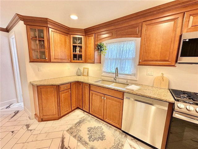 kitchen with appliances with stainless steel finishes, marble finish floor, a sink, light stone counters, and brown cabinets