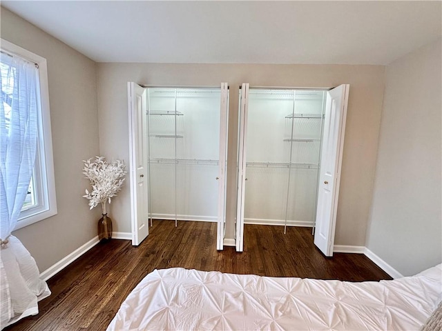 bedroom featuring baseboards, multiple windows, two closets, and wood finished floors