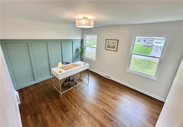 office area with visible vents, baseboards, a decorative wall, dark wood-type flooring, and a wainscoted wall