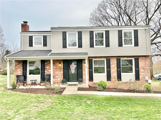 view of front facade featuring a front yard, brick siding, a chimney, and a shingled roof