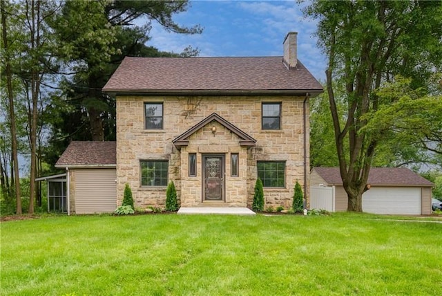 colonial-style house featuring a shingled roof, a detached garage, stone siding, a chimney, and a front lawn