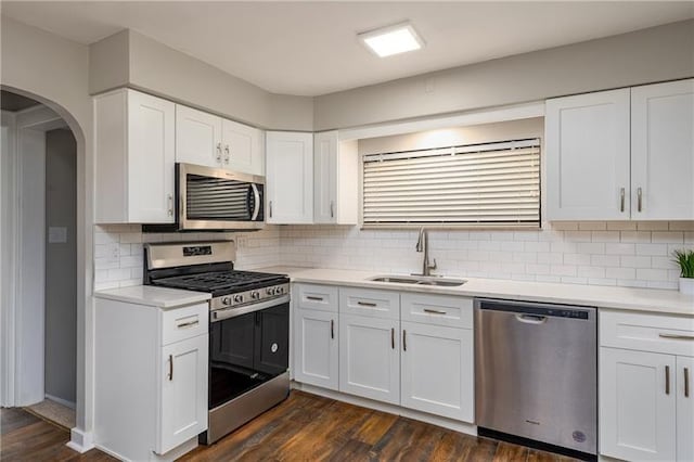 kitchen featuring arched walkways, a sink, dark wood-style flooring, light countertops, and appliances with stainless steel finishes