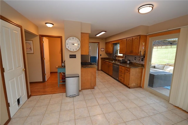 kitchen featuring tasteful backsplash, dishwasher, a sink, dark countertops, and brown cabinets