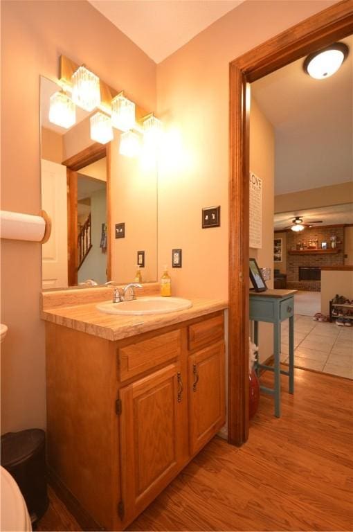 bathroom featuring wood finished floors, vanity, a ceiling fan, and a brick fireplace