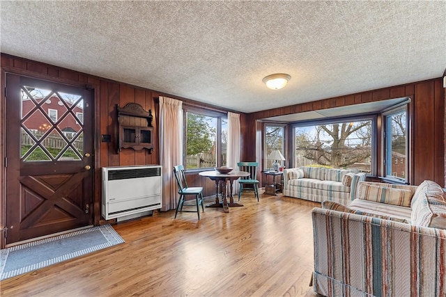 living room featuring wooden walls, heating unit, wood finished floors, and a textured ceiling