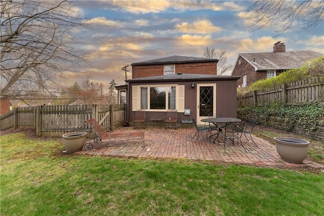 back of property at dusk featuring a patio, a yard, a fenced backyard, and an outdoor structure