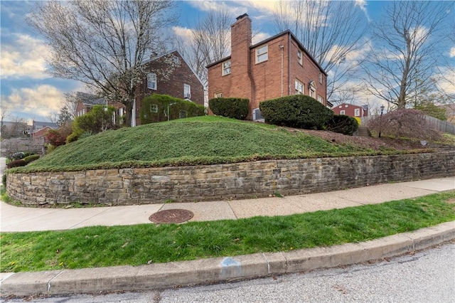 view of side of property with a yard, brick siding, and a chimney