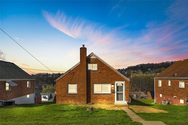 back of house featuring brick siding, central AC, a lawn, and a chimney