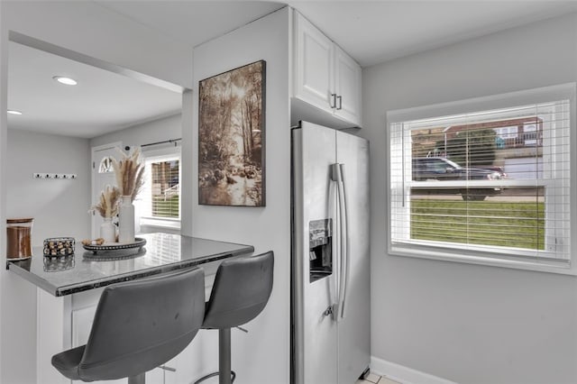 kitchen with white cabinets, baseboards, stainless steel refrigerator with ice dispenser, a kitchen breakfast bar, and recessed lighting
