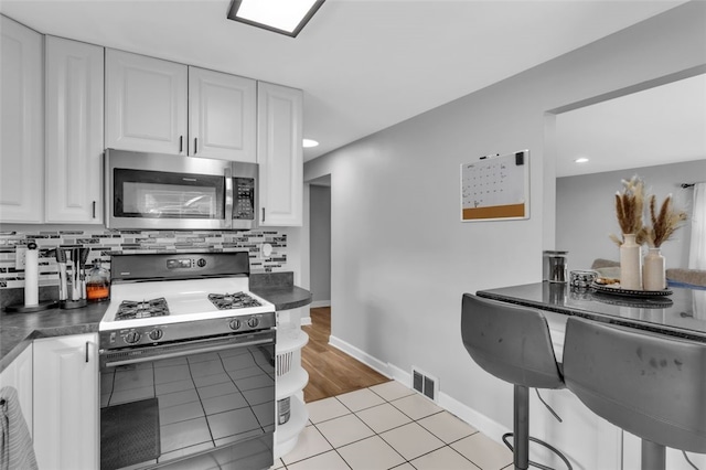kitchen featuring dark countertops, stainless steel microwave, range with gas stovetop, and white cabinetry