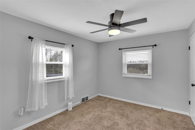 carpeted empty room with visible vents, baseboards, a ceiling fan, and plenty of natural light
