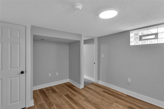below grade area with baseboards, a textured ceiling, and wood finished floors