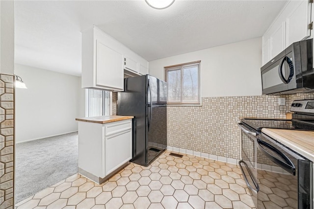 kitchen with white cabinets, black appliances, wainscoting, and wooden counters