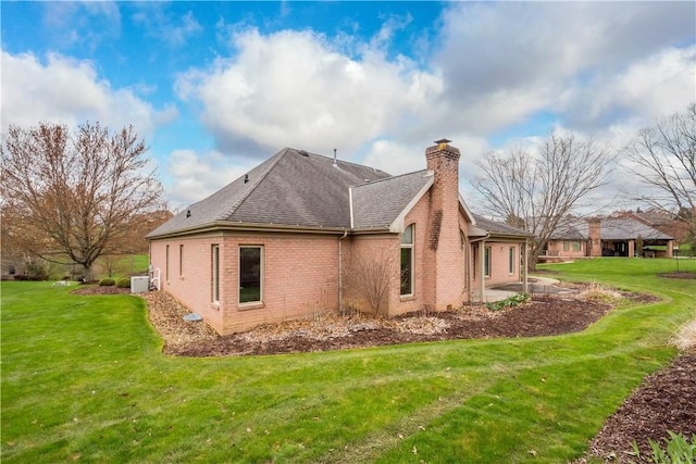 view of side of property with roof with shingles, a patio, brick siding, and a lawn