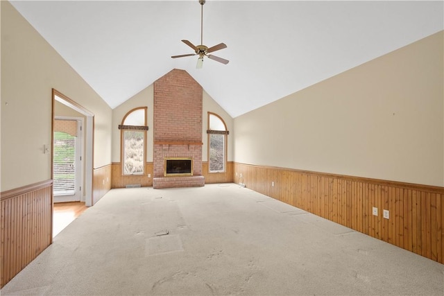 unfurnished living room with a ceiling fan, carpet, wooden walls, wainscoting, and lofted ceiling