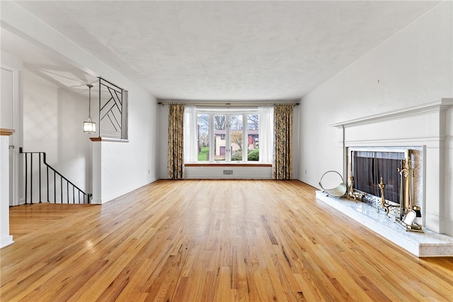 unfurnished living room with light wood-type flooring, baseboards, and a fireplace with raised hearth