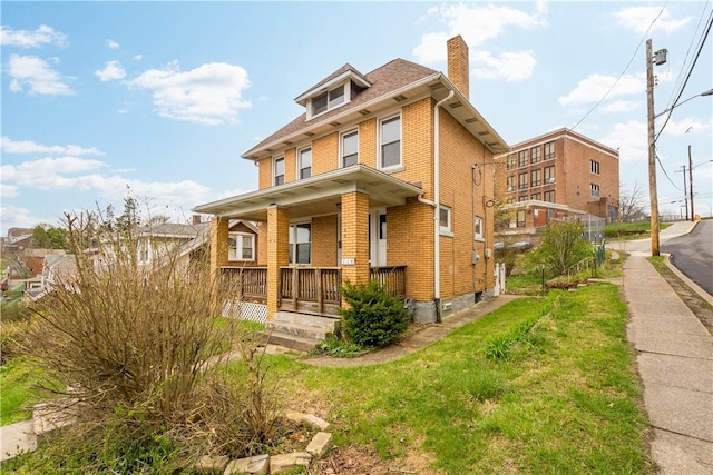 american foursquare style home featuring brick siding, covered porch, and a chimney