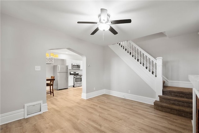 unfurnished living room with visible vents, baseboards, ceiling fan, stairway, and light wood-style flooring