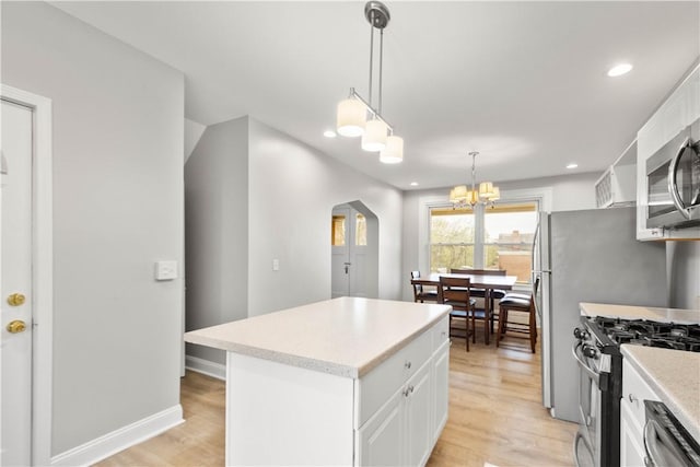 kitchen with arched walkways, light wood-style floors, a center island, and appliances with stainless steel finishes