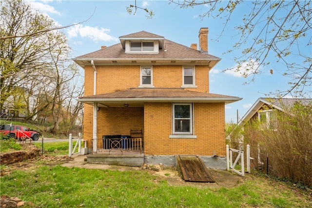 rear view of property featuring a porch, brick siding, a chimney, and a lawn