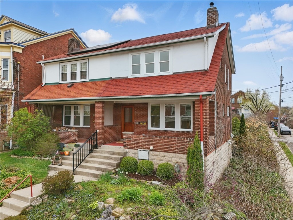 view of front of property with brick siding, solar panels, a chimney, and a shingled roof