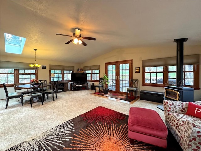 living area featuring a wood stove, ceiling fan, carpet, lofted ceiling with skylight, and french doors