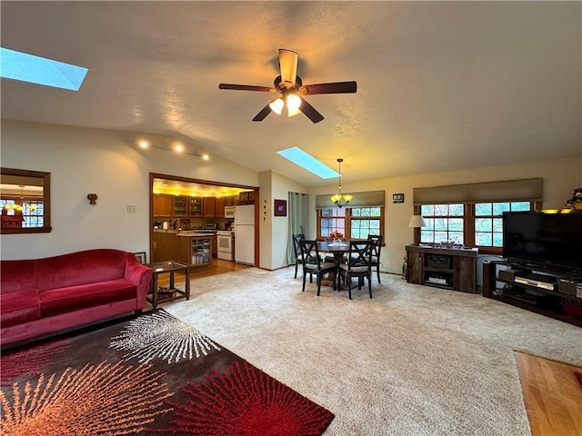 living room featuring vaulted ceiling with skylight, light colored carpet, and a ceiling fan