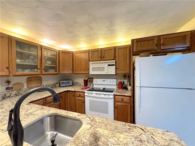 kitchen featuring brown cabinetry, a sink, white appliances, and glass insert cabinets