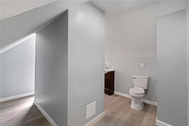 bathroom featuring baseboards, toilet, vanity, vaulted ceiling, and wood finished floors