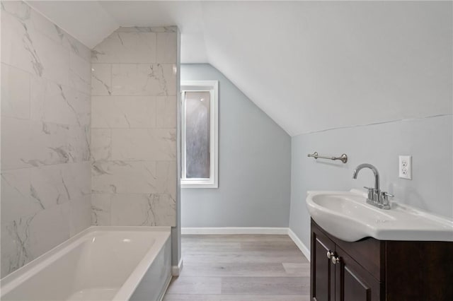 full bathroom with baseboards, vanity, a bathtub, wood finished floors, and lofted ceiling