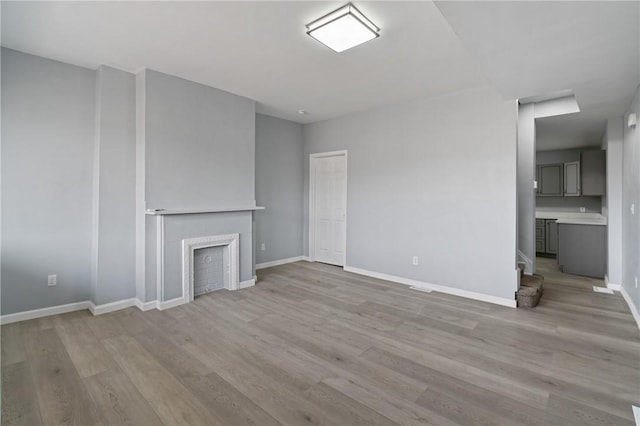 unfurnished living room featuring baseboards, a tile fireplace, wood finished floors, and stairs