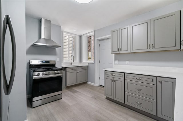 kitchen with wall chimney exhaust hood, a sink, light wood-style floors, gray cabinetry, and stainless steel appliances