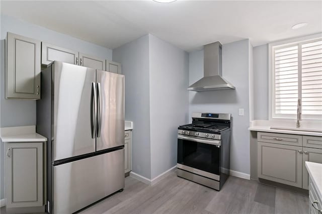 kitchen featuring stainless steel appliances, gray cabinetry, wall chimney exhaust hood, and a sink