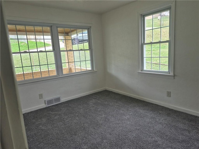 unfurnished room featuring dark carpet, a healthy amount of sunlight, baseboards, and visible vents