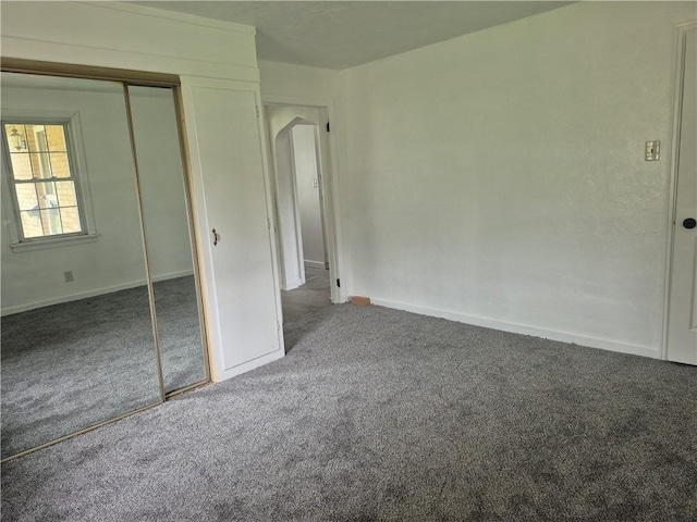 unfurnished bedroom featuring arched walkways, a closet, baseboards, and carpet floors