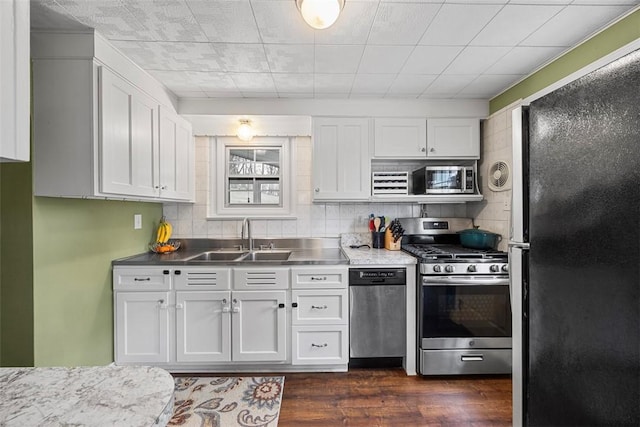 kitchen with a sink, stainless steel countertops, dark wood finished floors, white cabinetry, and stainless steel appliances