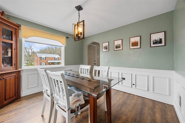 dining area featuring a wainscoted wall, arched walkways, a chandelier, and wood finished floors