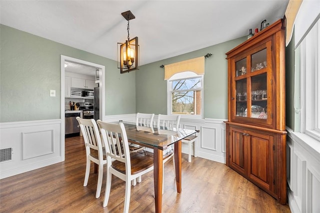 dining area featuring visible vents, a decorative wall, a chandelier, light wood-style floors, and a wainscoted wall
