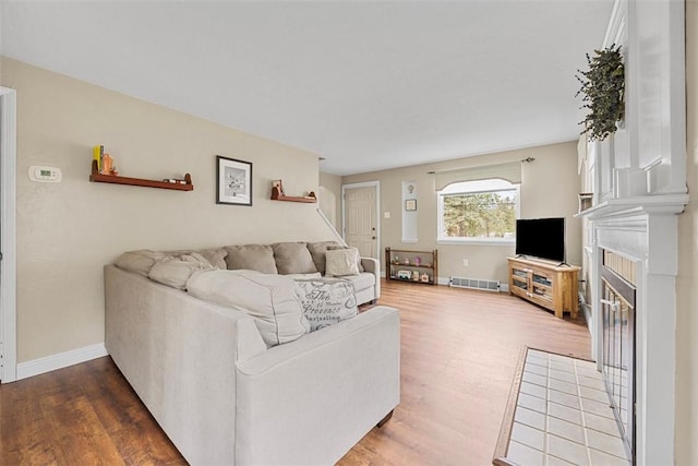living room with a fireplace with flush hearth, visible vents, baseboards, and wood finished floors