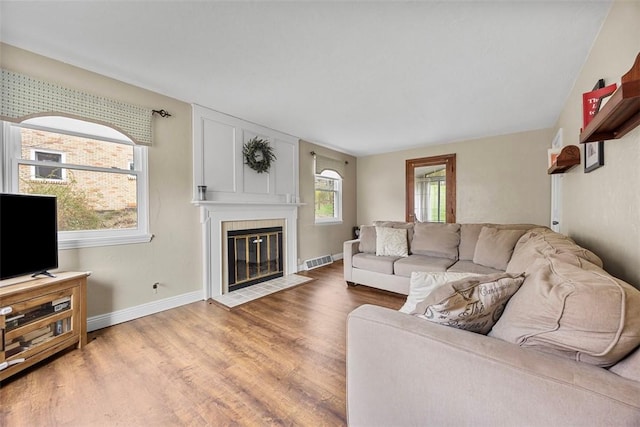 living room with a tiled fireplace, visible vents, baseboards, and light wood-style floors