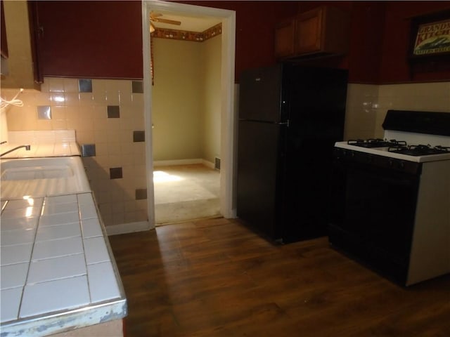 kitchen with a sink, freestanding refrigerator, dark wood-style floors, tile countertops, and gas range oven