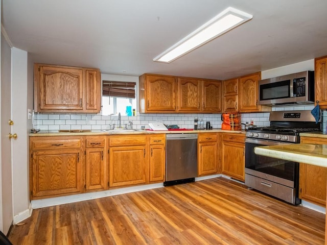 kitchen with a sink, light countertops, stainless steel appliances, backsplash, and light wood-style flooring