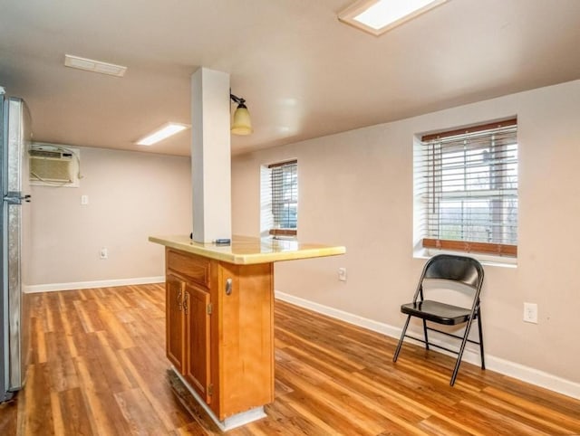kitchen featuring light wood-style flooring, a wall mounted air conditioner, baseboards, and brown cabinetry
