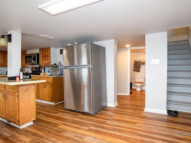 kitchen featuring light countertops, light wood-type flooring, baseboards, and appliances with stainless steel finishes