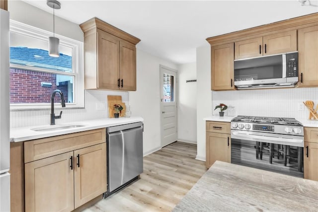 kitchen featuring light wood-style flooring, light countertops, decorative backsplash, stainless steel appliances, and a sink
