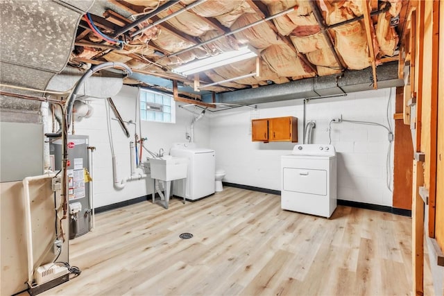 below grade area featuring light wood-style floors, water heater, separate washer and dryer, and a sink