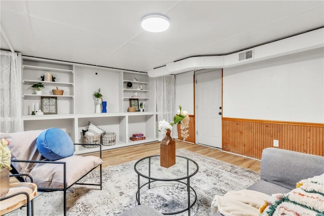 living area featuring built in features, wooden walls, a wainscoted wall, visible vents, and wood finished floors