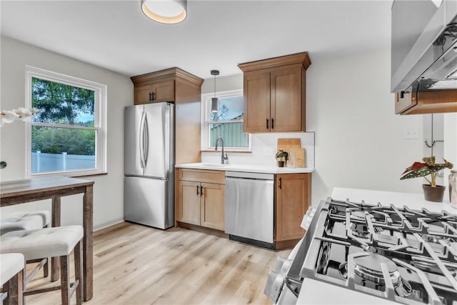 kitchen with decorative backsplash, appliances with stainless steel finishes, a sink, light countertops, and light wood finished floors